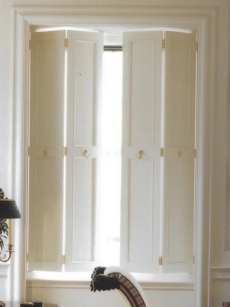 Restored panelled timber shutters with brass catches folded across a sash window